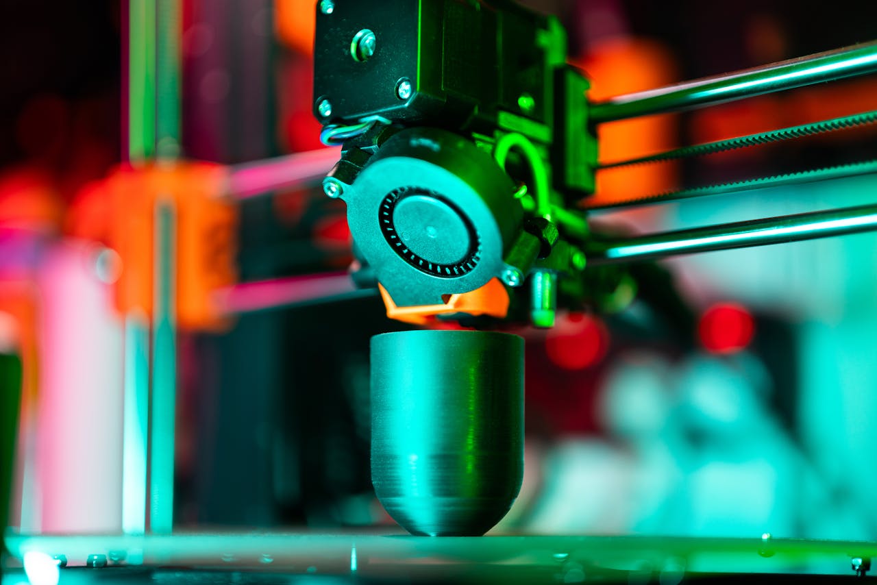 heros-img Close-up of a 3D printer creating a product in neon lighting.