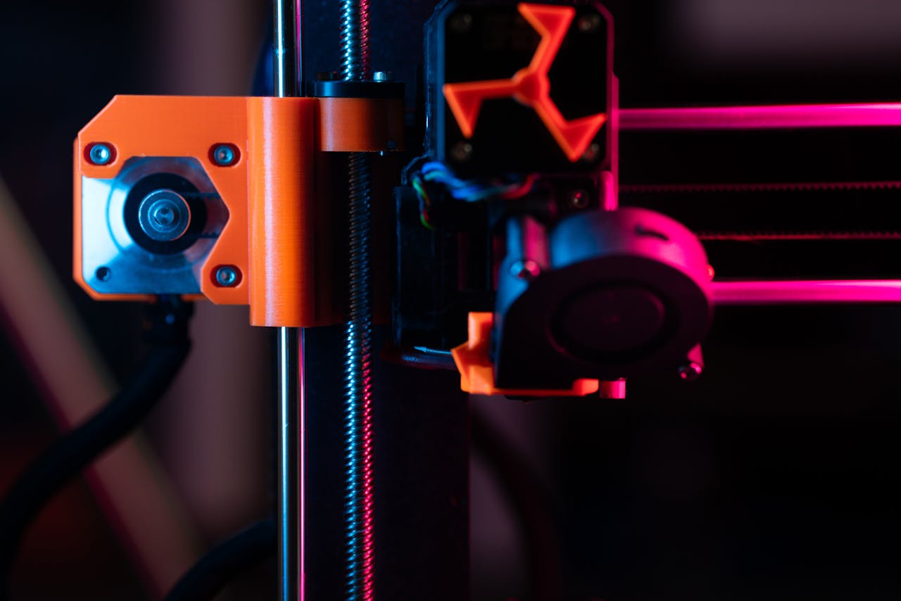 about-us-02 A detailed close-up of a 3D printer showcasing its extruder and components under vibrant lighting.
