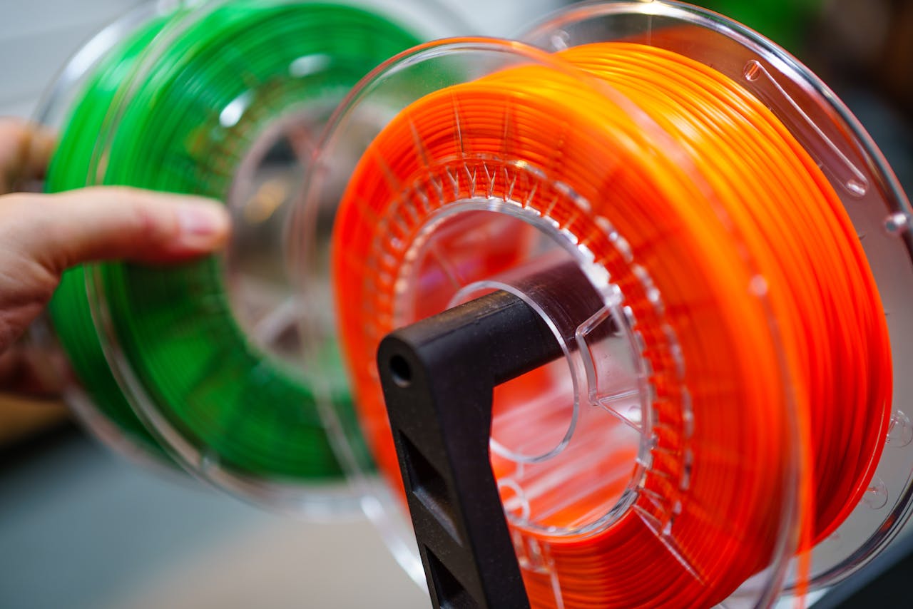 about-us-01 Vibrant orange and green 3D printer filament spools for innovative manufacturing uses.